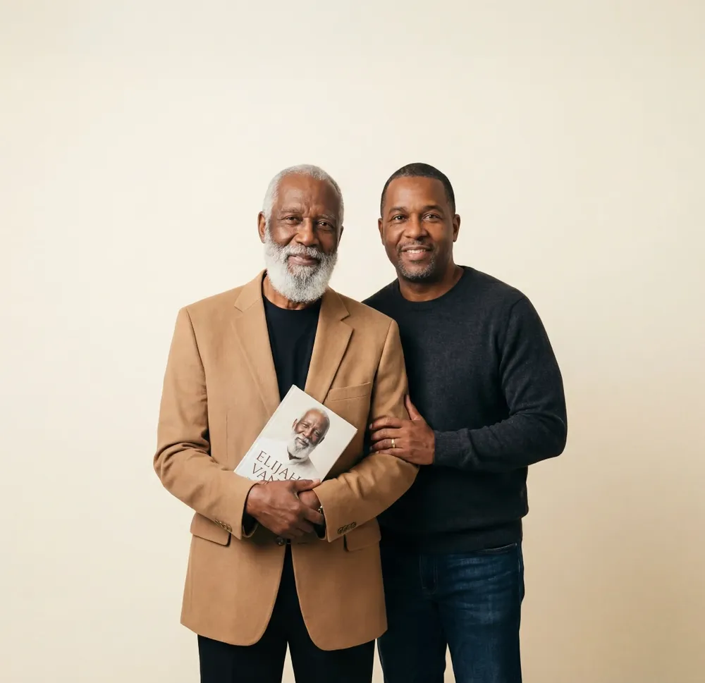 An older man holding his finished hardcover, his grown son beside him
